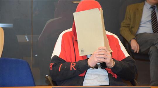 Der Angeklagte im Baggersee-Mordprozess vor dem Landgericht Stade verdeckt sein Gesicht hinter Büropappe.